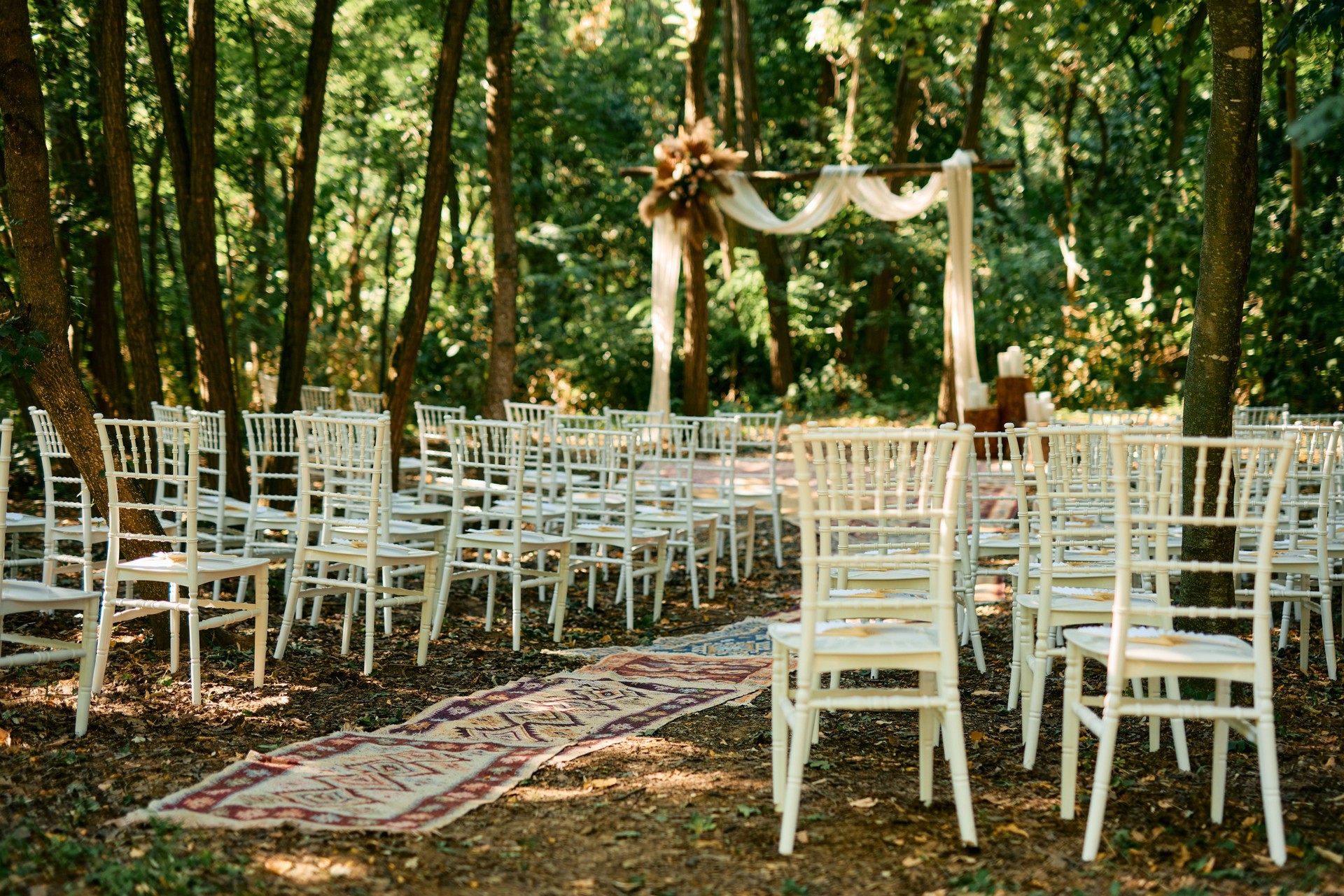 Wedding ceremony setup in the forest with white chairs and carpet